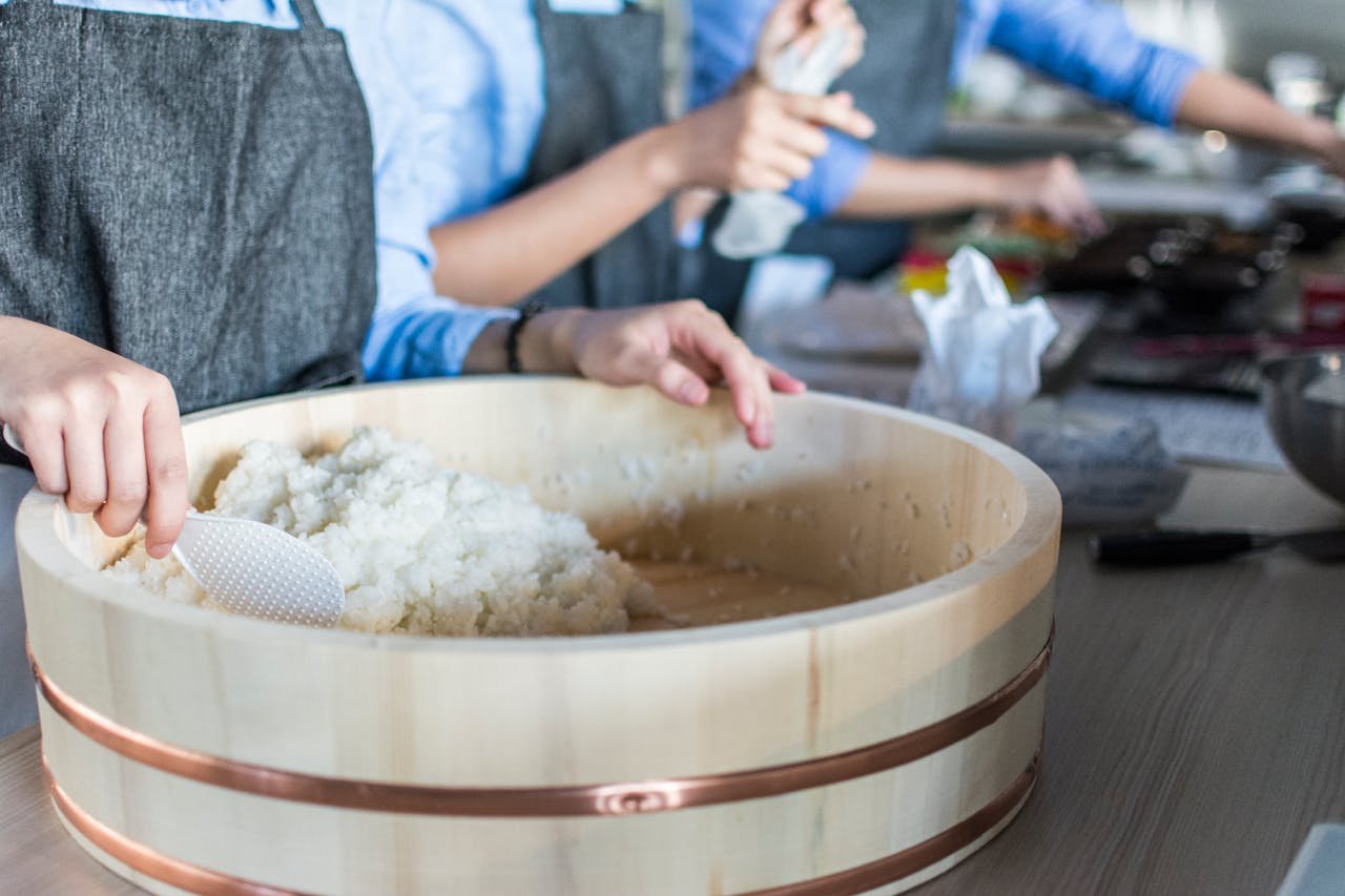 Close-up of sushi rice being prepared by chefs in a bright modern kitchen setting.