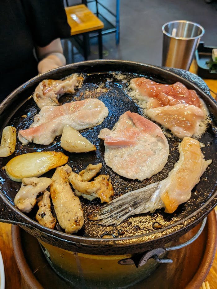 A rustic meal of assorted meats and vegetables grilling on a pan indoors.