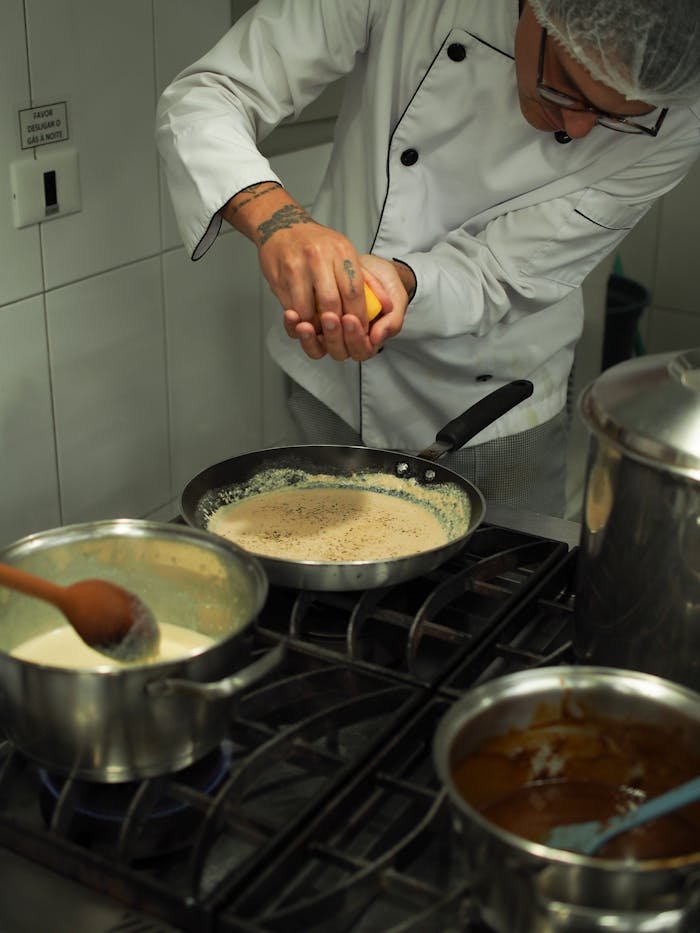 Chef carefully preparing sauce with citrus in a bustling kitchen setting.